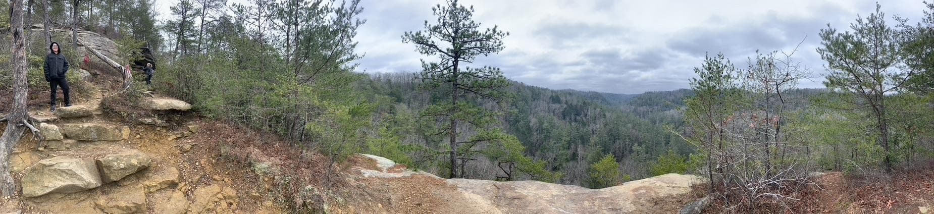 Plan your vacation to the red river gorge in Kentucky – rent a cabin Hikers at Red River Gorge, KY overlook a forested valley. Adventure in Kentucky!