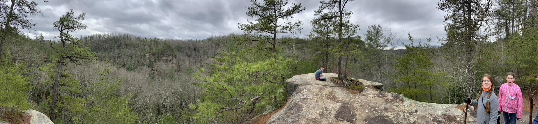 Scenic overlook in Red River Gorge, KY, with hikers on a rock. Explore Clifty Wilderness Area with fun mystery hikes!